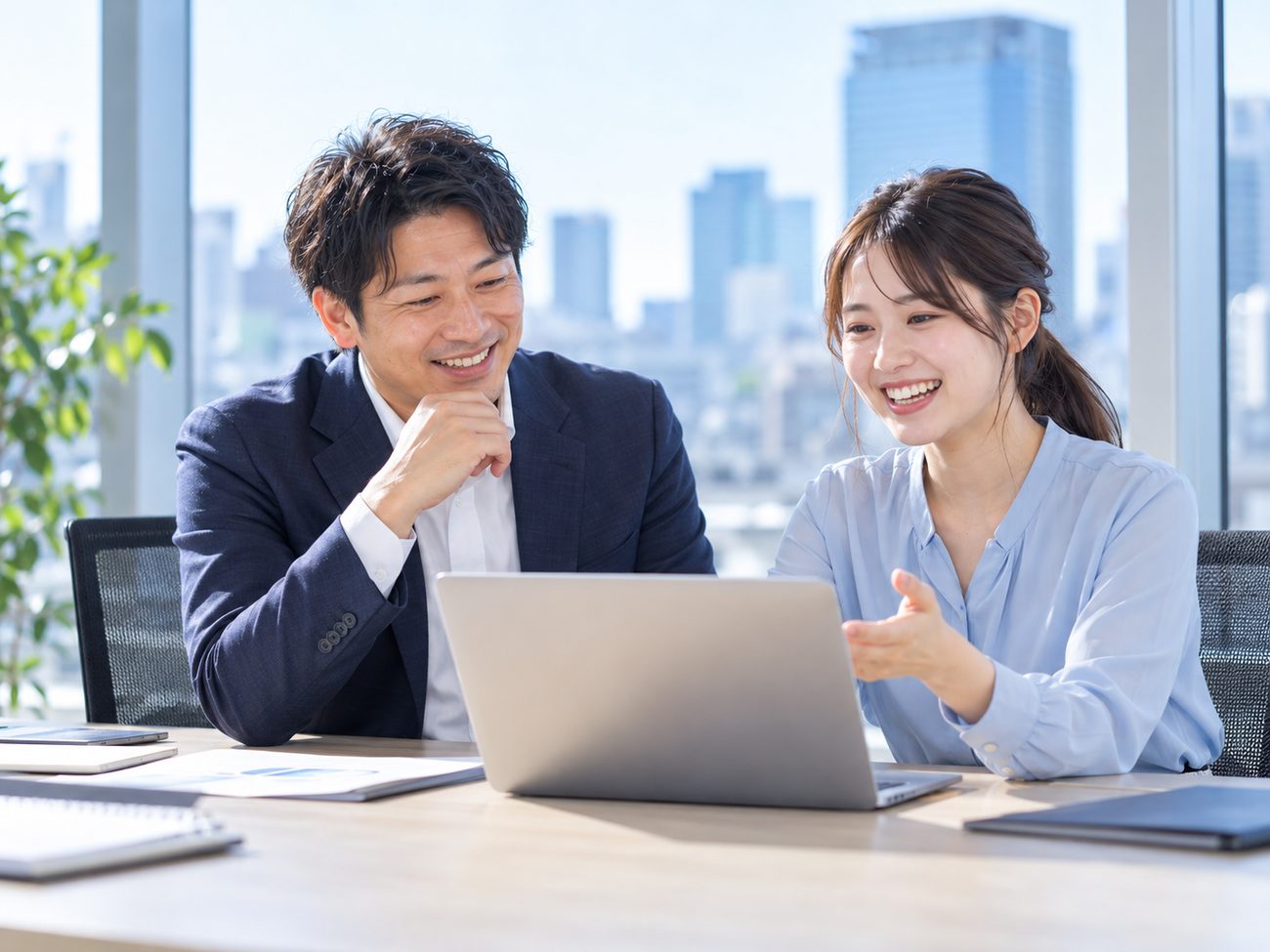 ノートパソコンを見ながら笑顔で打ち合わせするビジネスパーソン2人